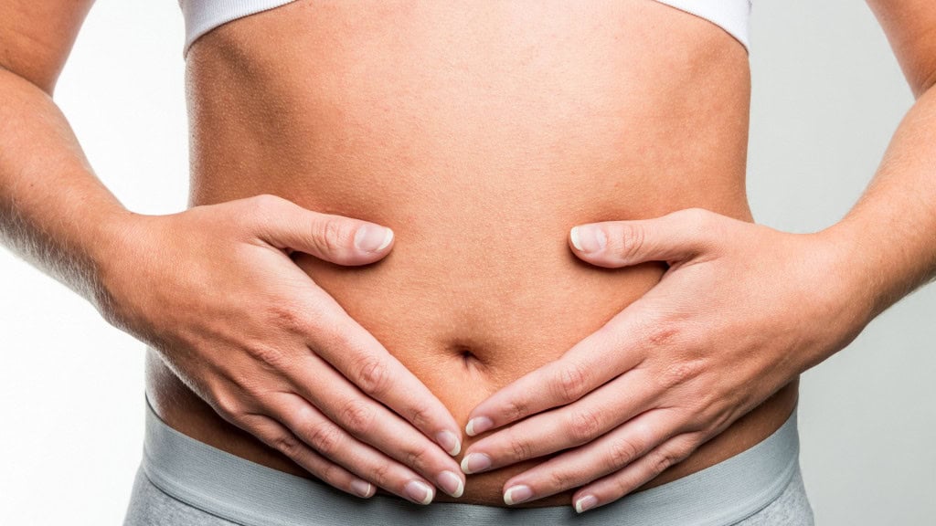 Mulher com as duas mãos sobre a barriga na região do útero e do intestino