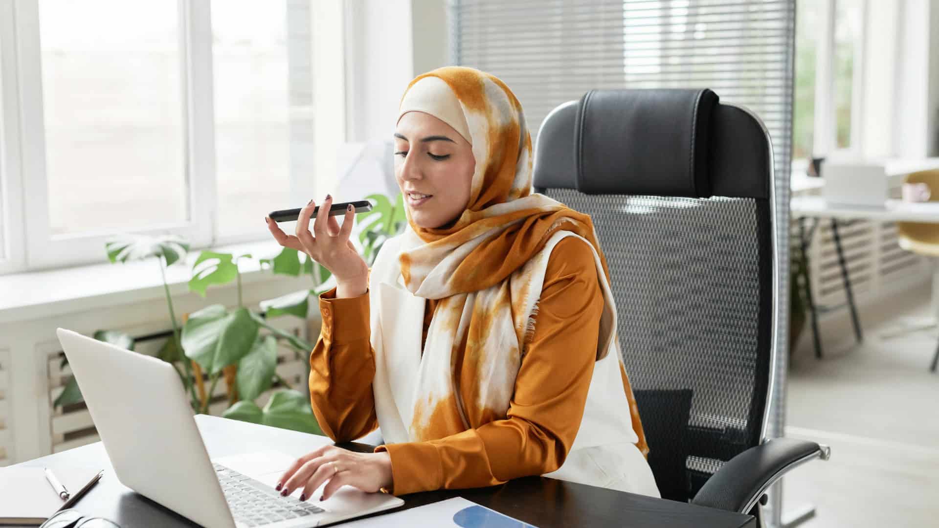 Mulher falando no celular enquanto usa o computador