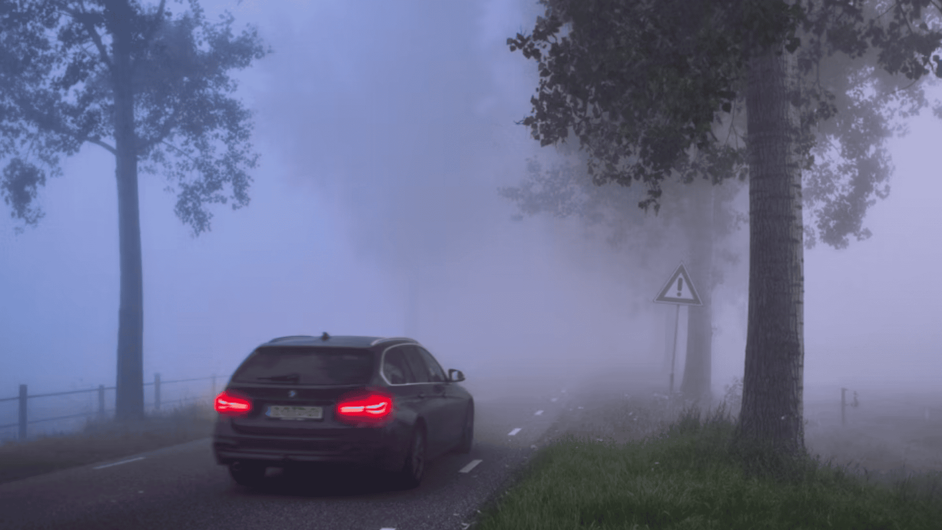 Traseira do carro com faróis ligados passando em estrada com nevoeiro