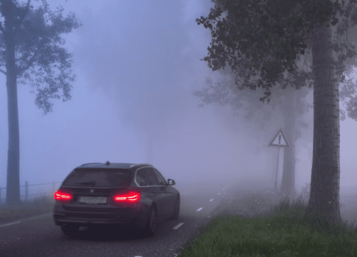 Traseira do carro com faróis ligados passando em estrada com nevoeiro