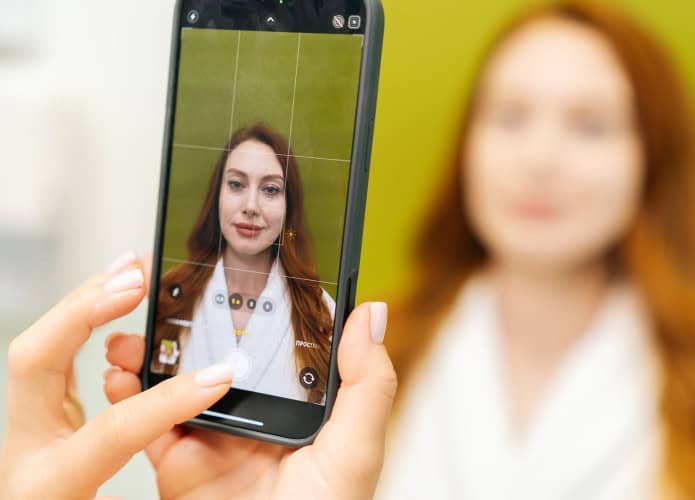 Close-up de um cosmetologista usando um smartphone para tirar a foto de uma mulher antes do procedimento estético, registrando a aparência atual para comparação e documentação na clínica. Conceito de tratamento de beleza.