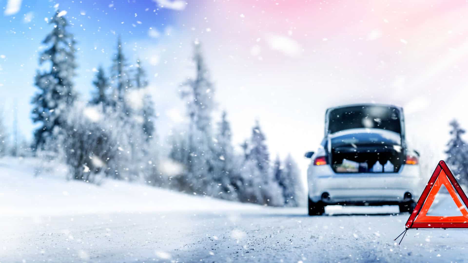 Um carro está parado em uma estrada nevada com o porta-malas aberto, sugerindo uma situação de emergência. Um triângulo de sinalização está posicionado atrás do veículo, alertando outros motoristas sobre o ocorrido.