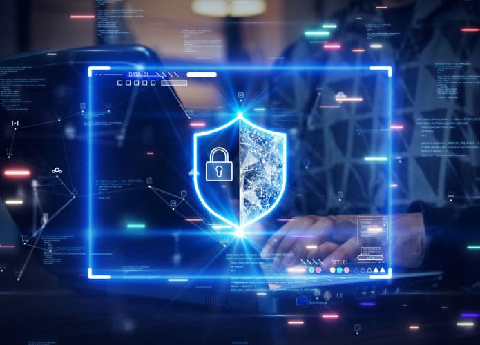 Montagem com ilustração digital de escudo de cibersegurança em cima de foto de pessoa digitando em computador