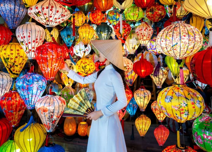 Mulher usando vestido azul e chapéu de palha tocando balão em local cheio de balões com estética chinesa
