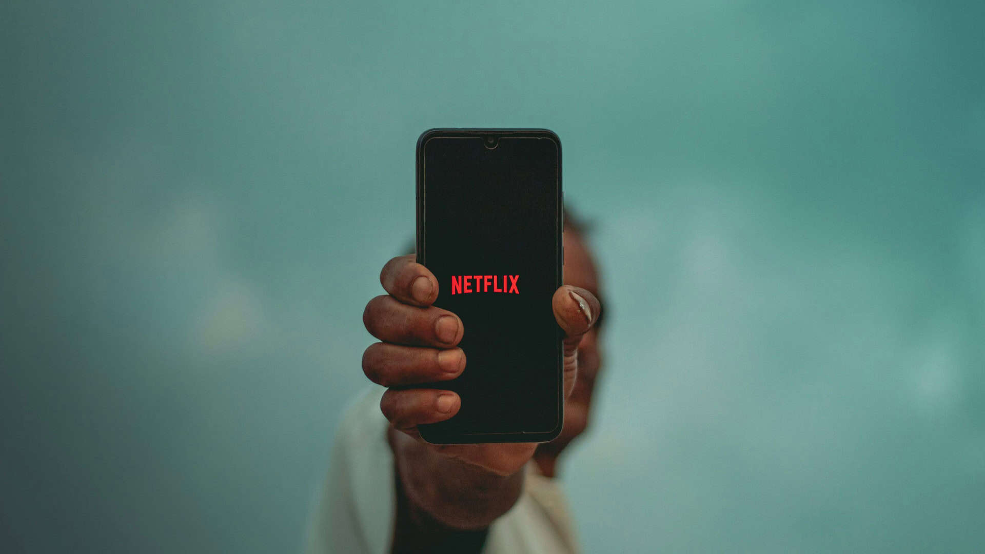 Pessoa mostrando um celular com logo da Netflix na tela