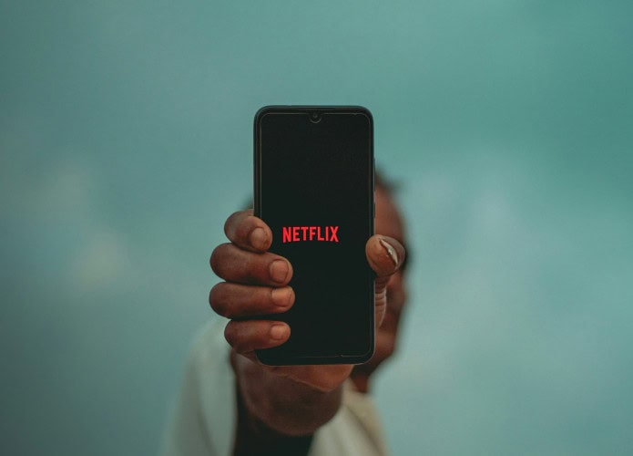 Pessoa mostrando um celular com logo da Netflix na tela