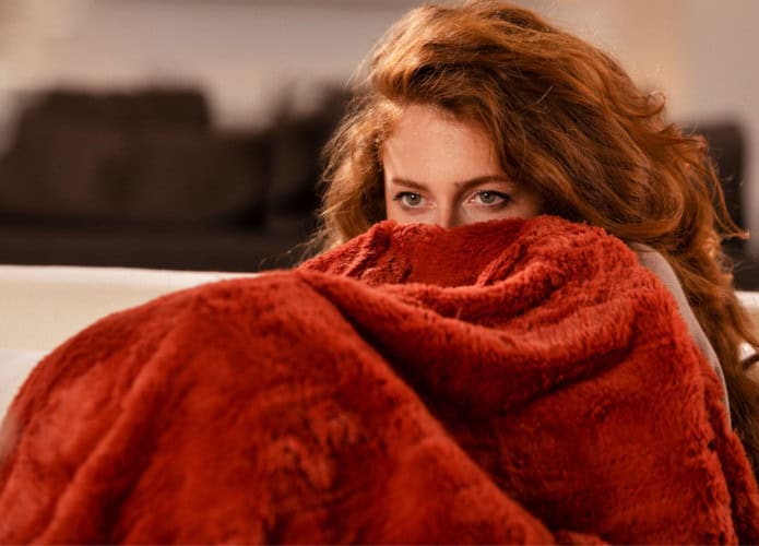 Mulher ruiva se protege com cobertor deixando apenas os olhos de fora