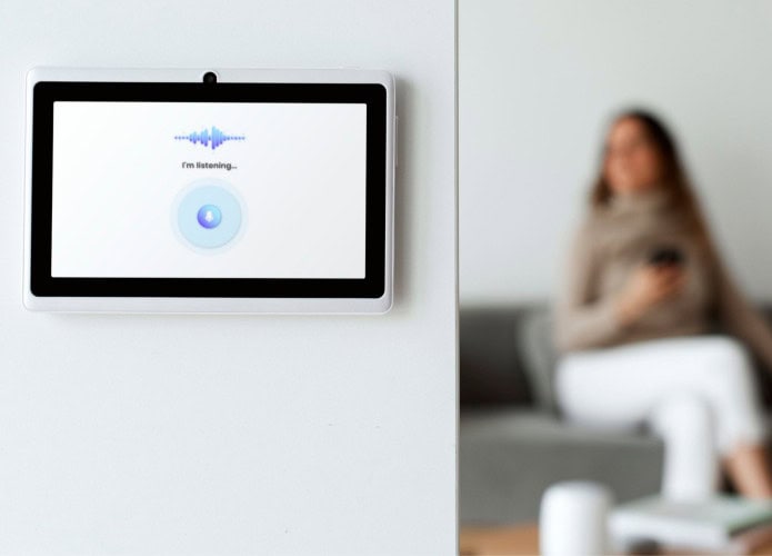 visão em primeiro plano de um monitor de casa inteligente, com mulher sentada em sofá em segundo plano, desfocada