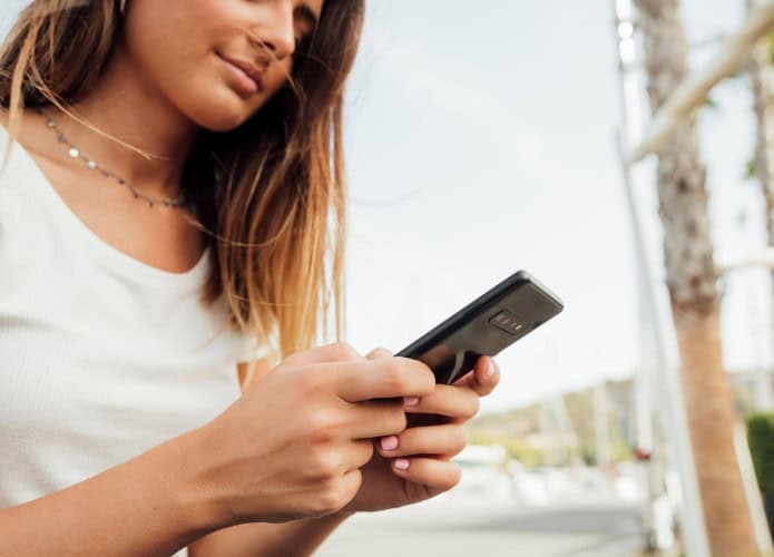 Mulher sentada em ambiente externo mexe no celular