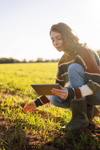Mulher agachada em uma plantação e olhando para um tablet