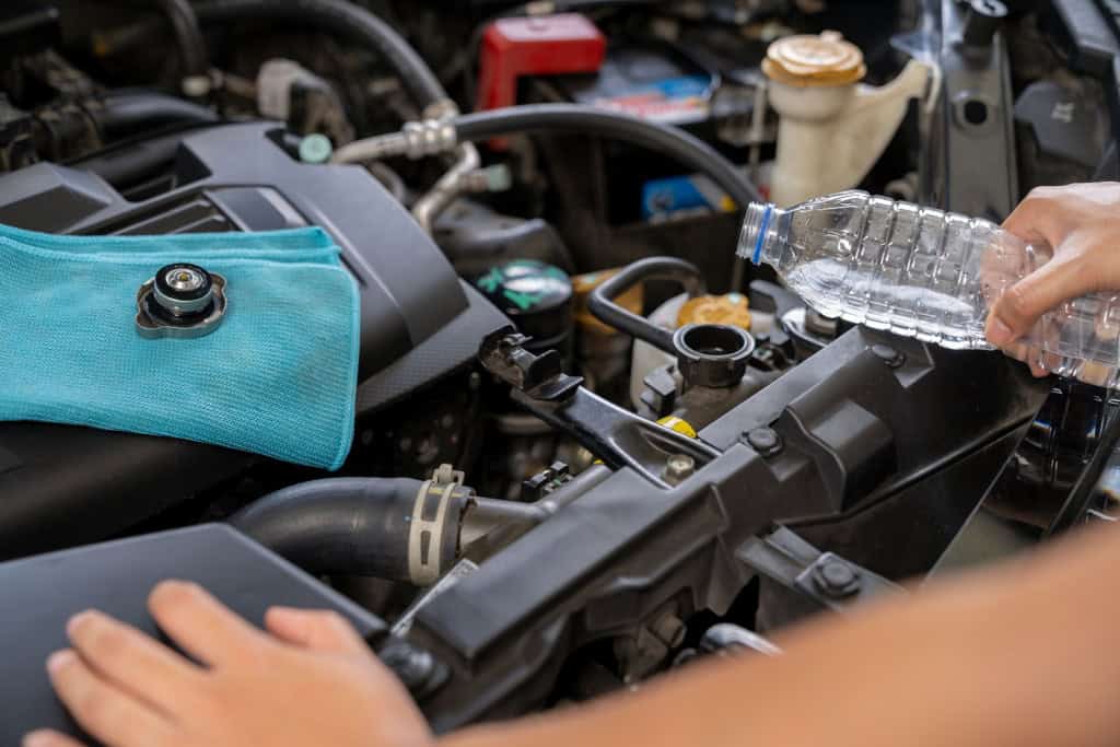 Imagem mostra pessoa colocando água no radiador de um carro