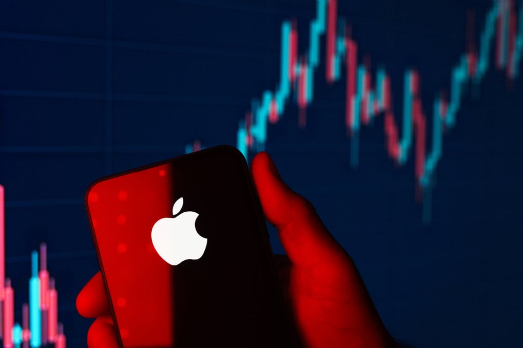 Logo da Apple em um smartphone com um gráfico financeiro ao fundo