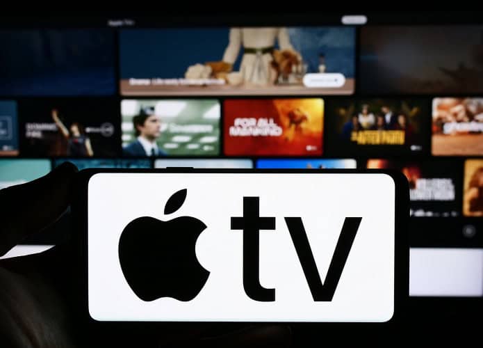 Ao fundo, desfocado, página inicial da Apple TV+; à frente, logo da Apple TV+ em um smartphone