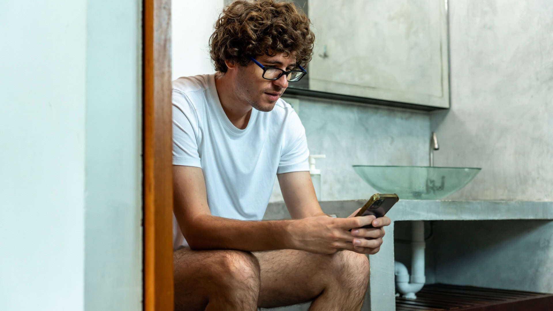 Homem sentado na privada (vaso sanitário) com o celular na mão