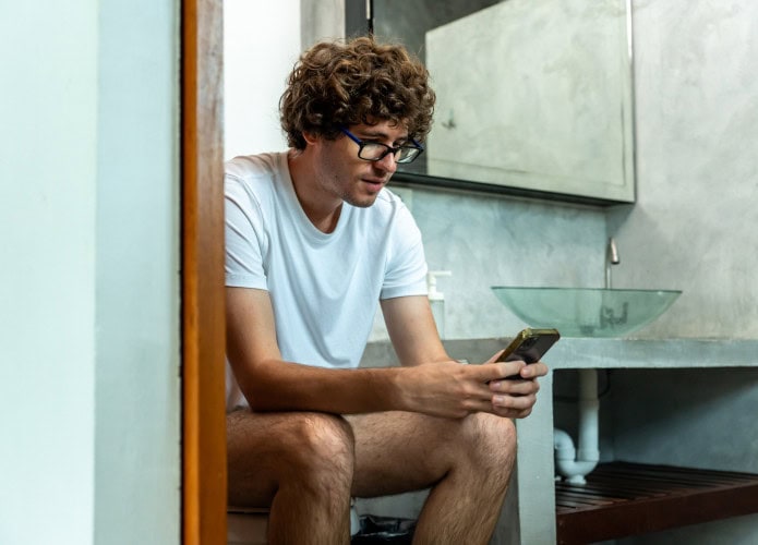 Homem sentado na privada (vaso sanitário) com o celular na mão