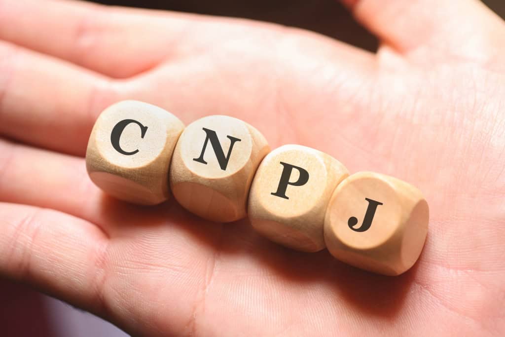 Letras CNPJ representadas em cubos de madeira sobre a mão de uma pessoa