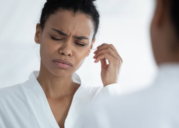 Mulher jovem tentando limpar os ouvidos com cotonete, sente dor e desconforto