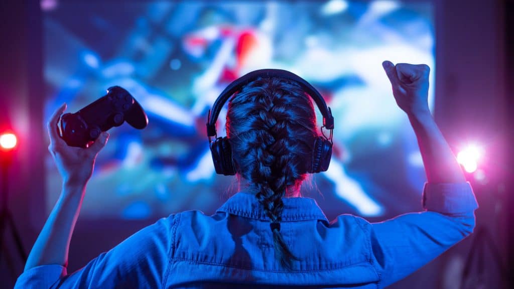 Garota com fones de ouvido joga videogame em uma tela grande com iluminação de néon