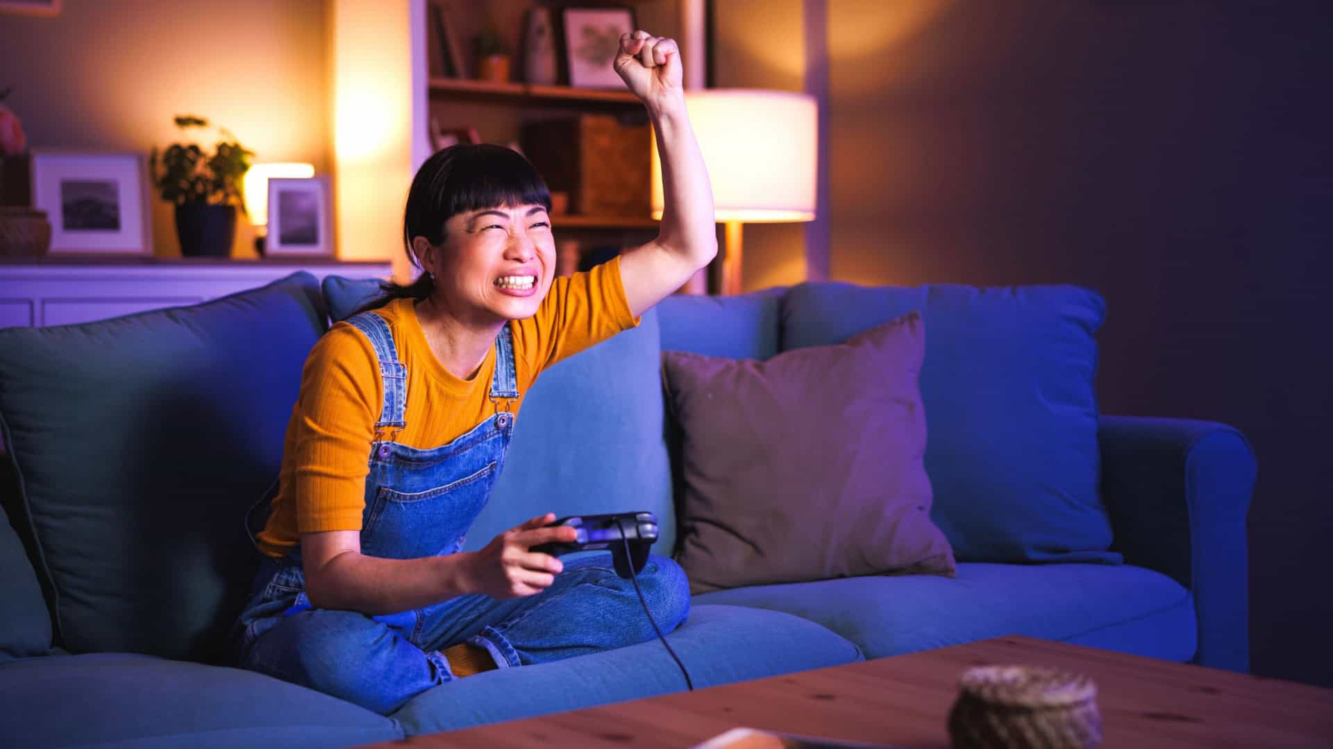 Mulher se diverte jogando videogame em casa tarde da noite, comemorando a vitória.