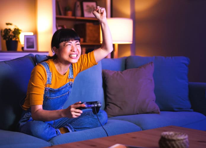Mulher se diverte jogando videogame em casa tarde da noite, comemorando a vitória.