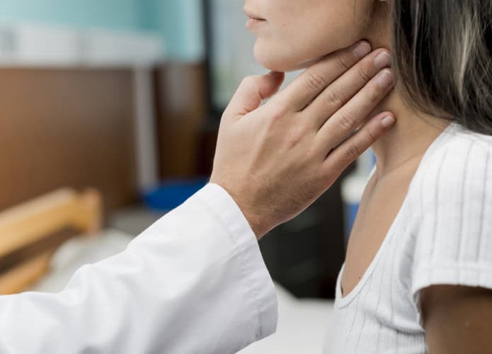 médico tocando a garganta de uma moça na região das amígdalas