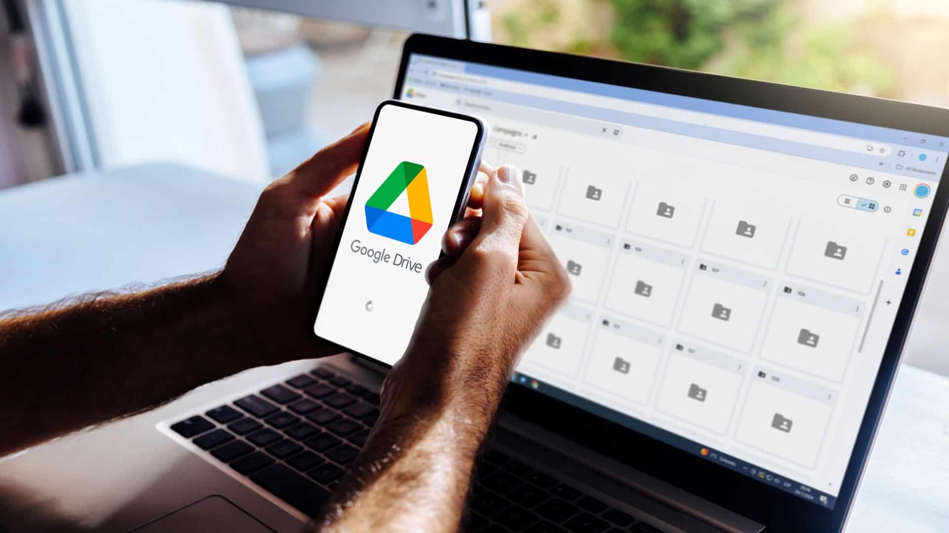 Imagem ilustrativa do Google Drive no celular e no computador. Homem segurando um smartphone com aplicativo de armazenamento em nuvem na tela