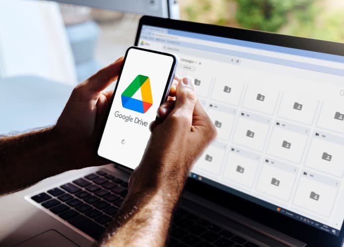 Imagem ilustrativa do Google Drive no celular e no computador. Homem segurando um smartphone com aplicativo de armazenamento em nuvem na tela