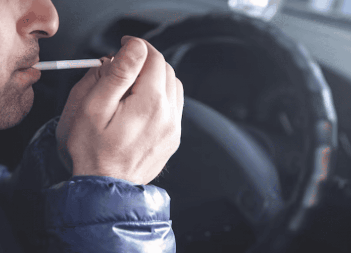 homem fumando um cigarro dentro do seu carro enquanto dirige