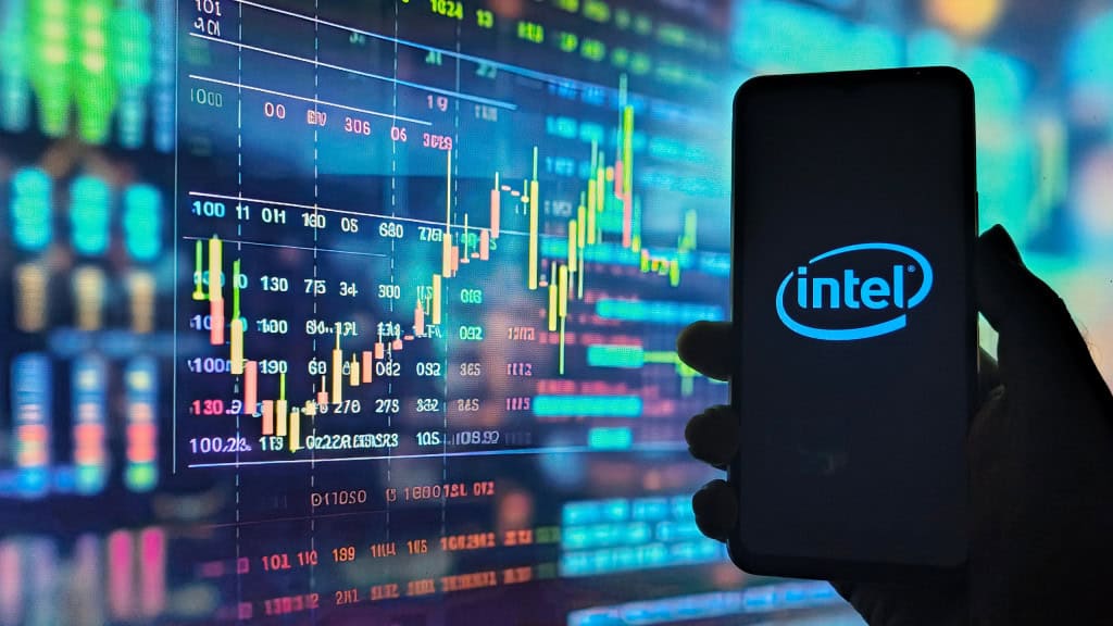 Logo da Intel em um smartphone; ao fundo, gráficos financeiros
