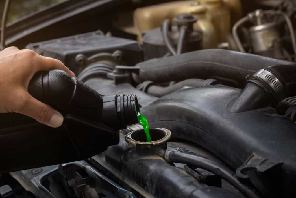 Imagem mostra mecânico abastecendo manualmente o radiador e o sistema de arrefecimento do carro com líquido de arrefecimento verde