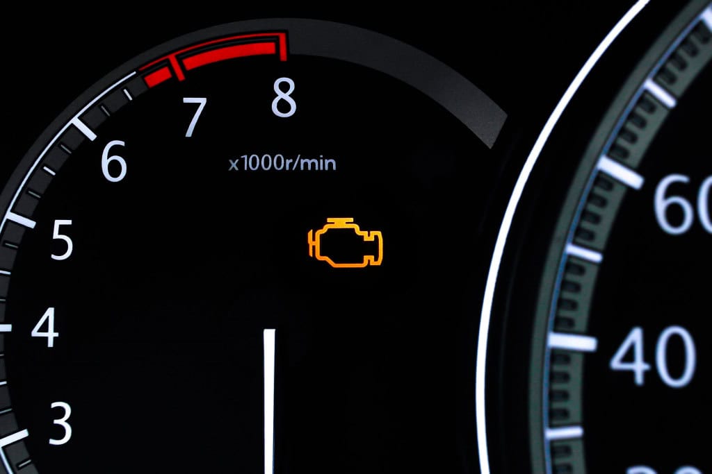 Imagem mostra closeup de um painel de um carro com uma luz de verificação do motor iluminada e o tacômetro exibindo rotações do motor por minuto