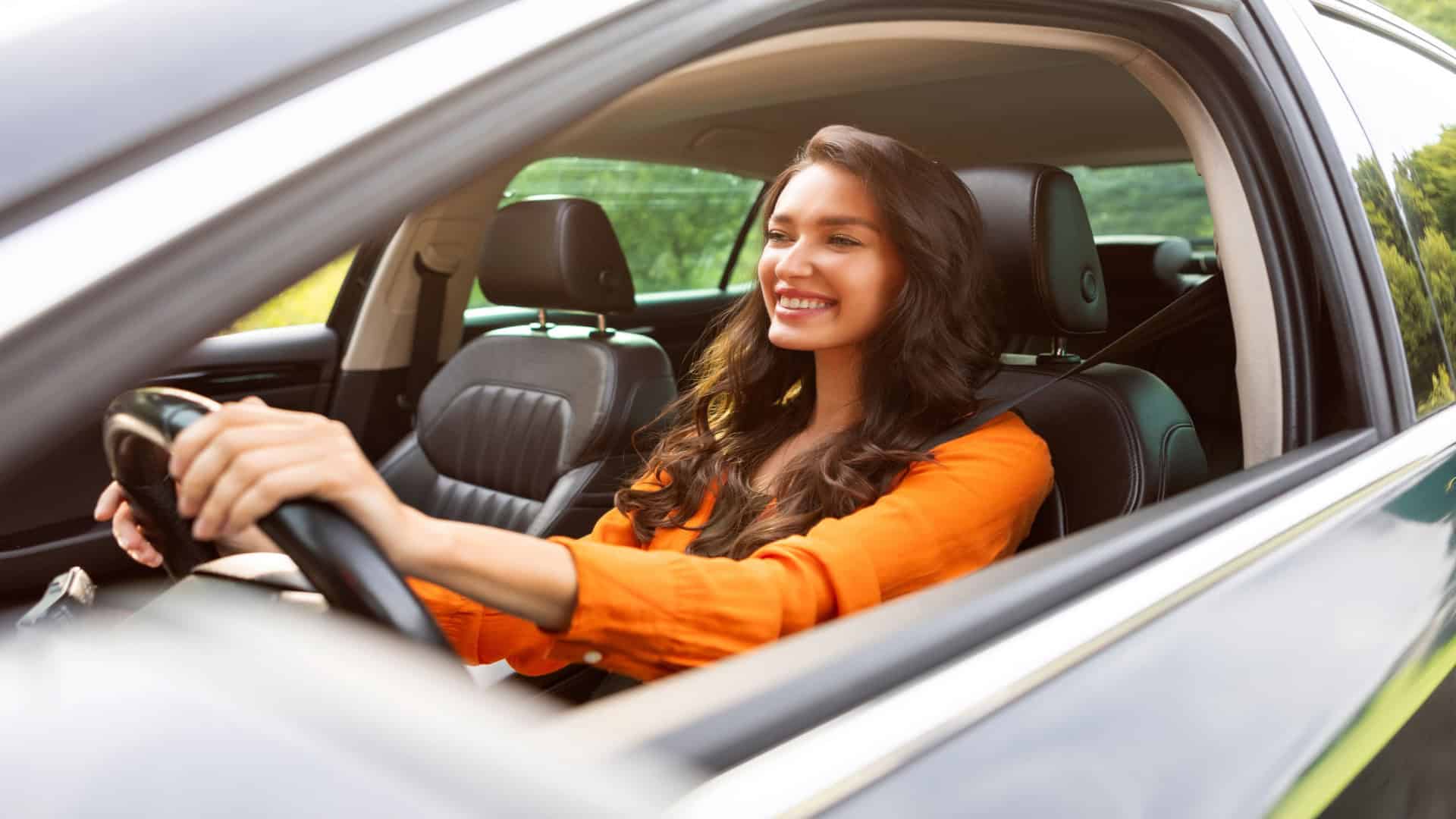 Imagem ilustrativa de mulher sorrindo ao volante e dirigindo carro