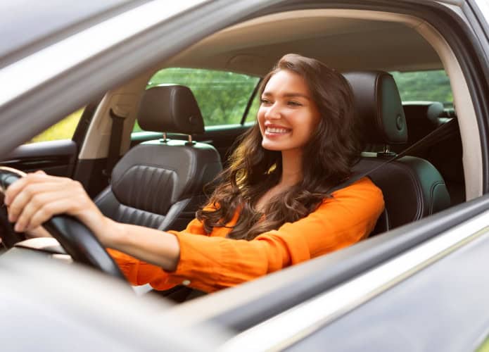 Imagem ilustrativa de mulher sorrindo ao volante e dirigindo carro