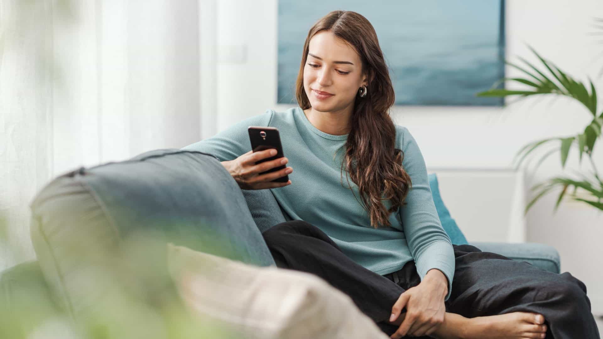 Mulher jovem usando o celular no sofá