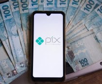 Notas de R$ 100 espalhadas; por cima, um smartphone com o logotipo do Pix