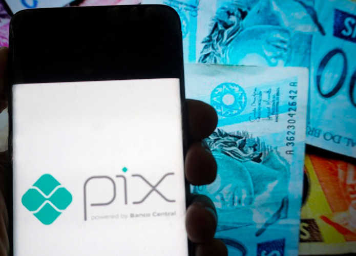 Ao fundo, notas de real; à frente, o logotipo do Pix em um smartphone