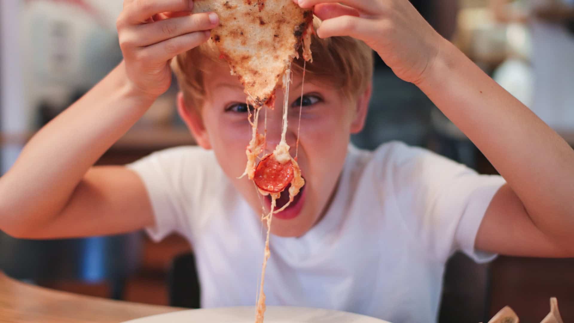 Garoto comendo pizza de calabresa com muito queijo derretido