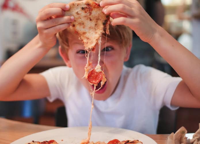Garoto comendo pizza de calabresa com muito queijo derretido