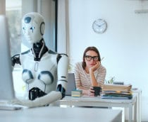 Robô, em primeiro plano, digitando em um teclado de computador; atrás, uma mulher olhando o robô com cara entediada