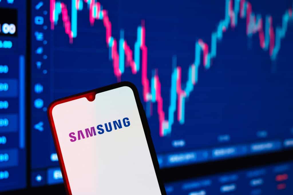 Ao fundo, desfocado, gráfico financeiro; à frente, logo da Samsung em um smartphone