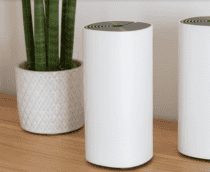 roteadores mesh em cima de uma mesa de madeira, com um vaso de plantas ao lado e uma parede branca atrás