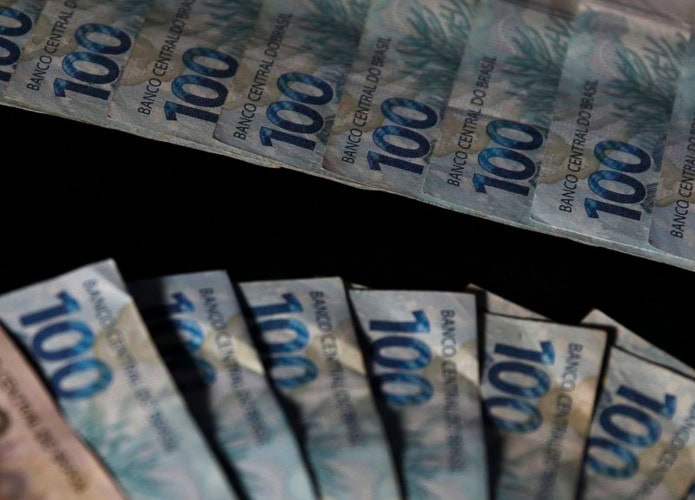 Notas de 100 e 200 reais organizadas em formatos de leque e fila numa mesa preta