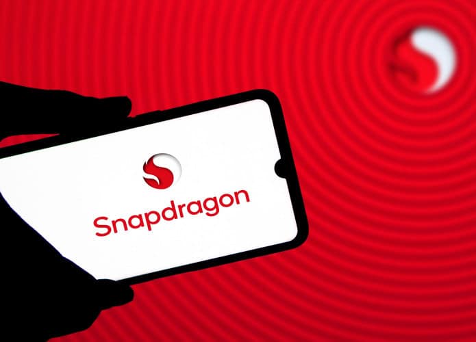 Pessoa segurando celular com logomarca do Snapdragon na tela; ao fundo, uma tela mostrando o logotipo da Qualcomm