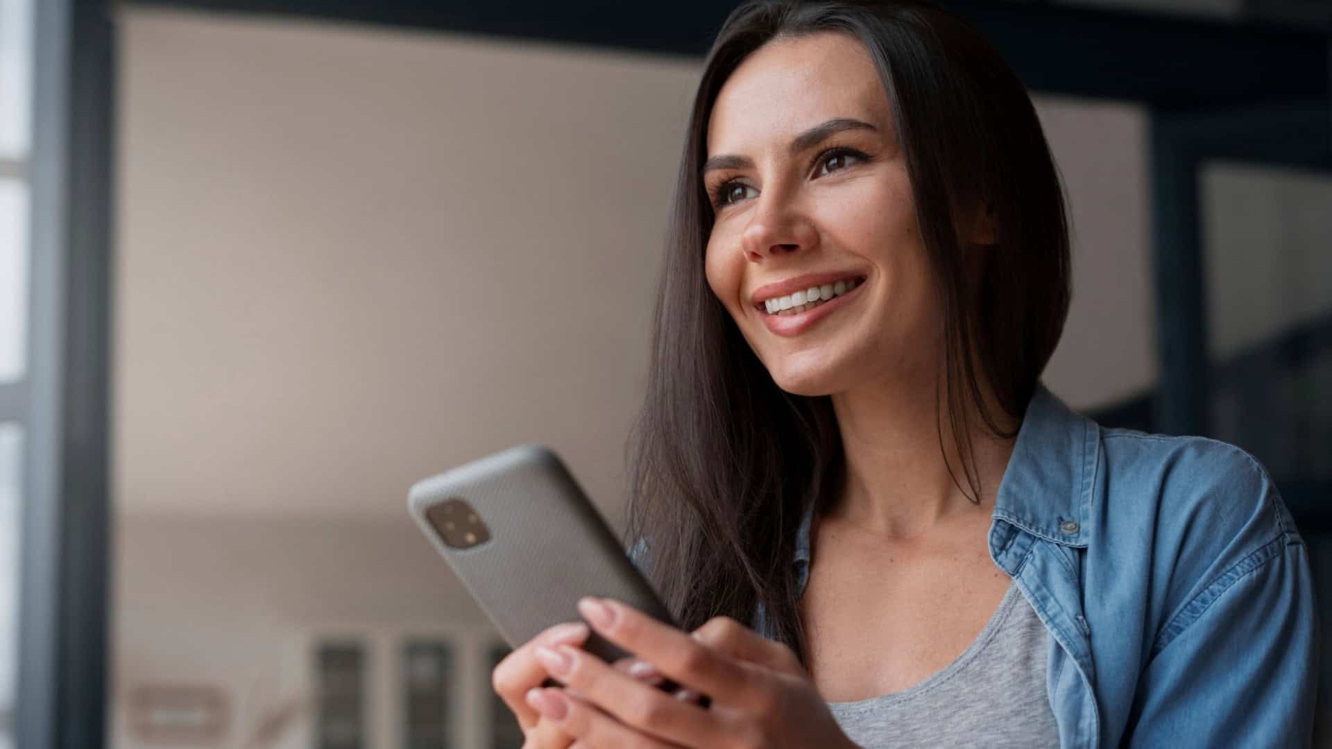 mulher sorri e olha enquanto segura celular