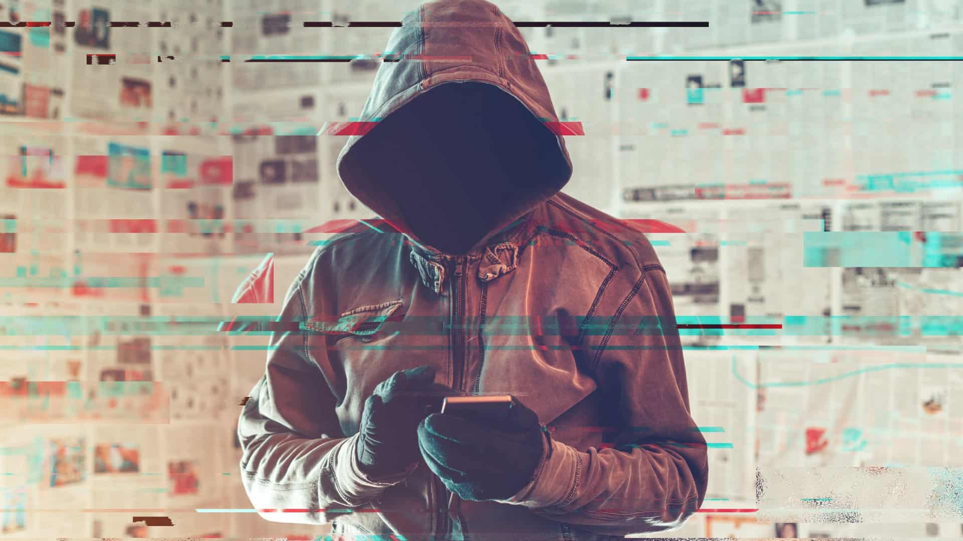 Pessoa com um capuz cobrindo cabeça e rosto com um celular nas mãos