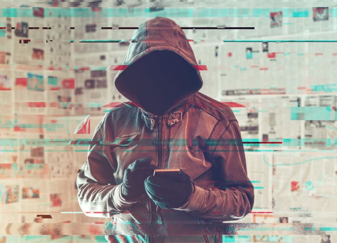 Pessoa com um capuz cobrindo cabeça e rosto com um celular nas mãos