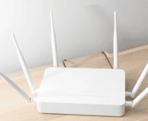 roteador branco em cima de uma mesa de madeira com uma parede cinza atrás