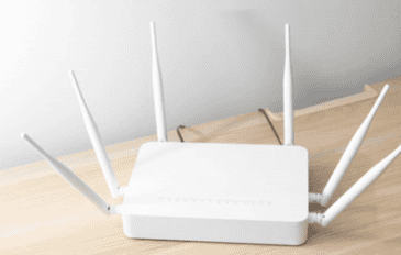 roteador branco em cima de uma mesa de madeira com uma parede cinza atrás