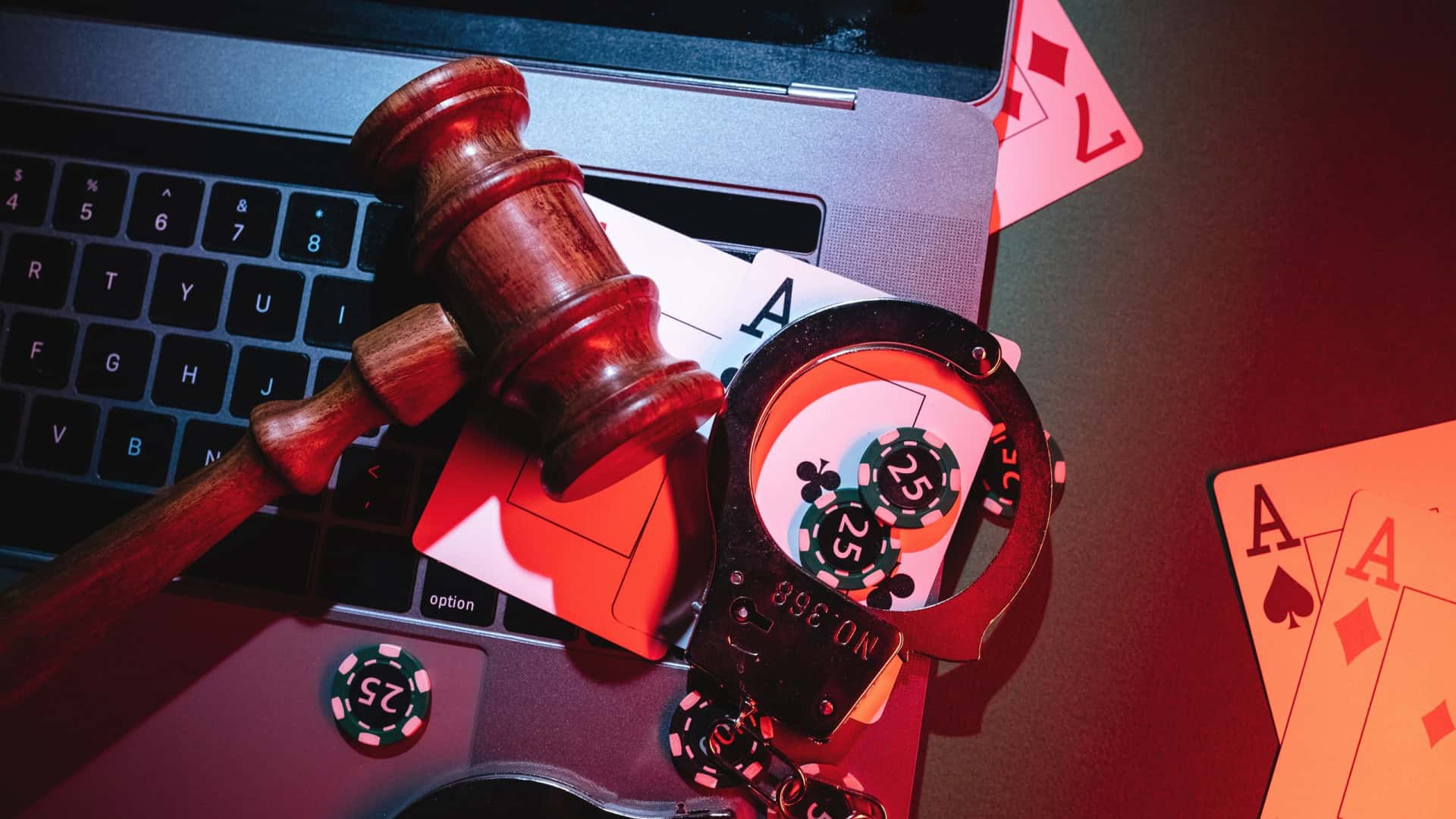 Martelo de juiz, cartas de baralho e um par de algemas em cima de um notebook
