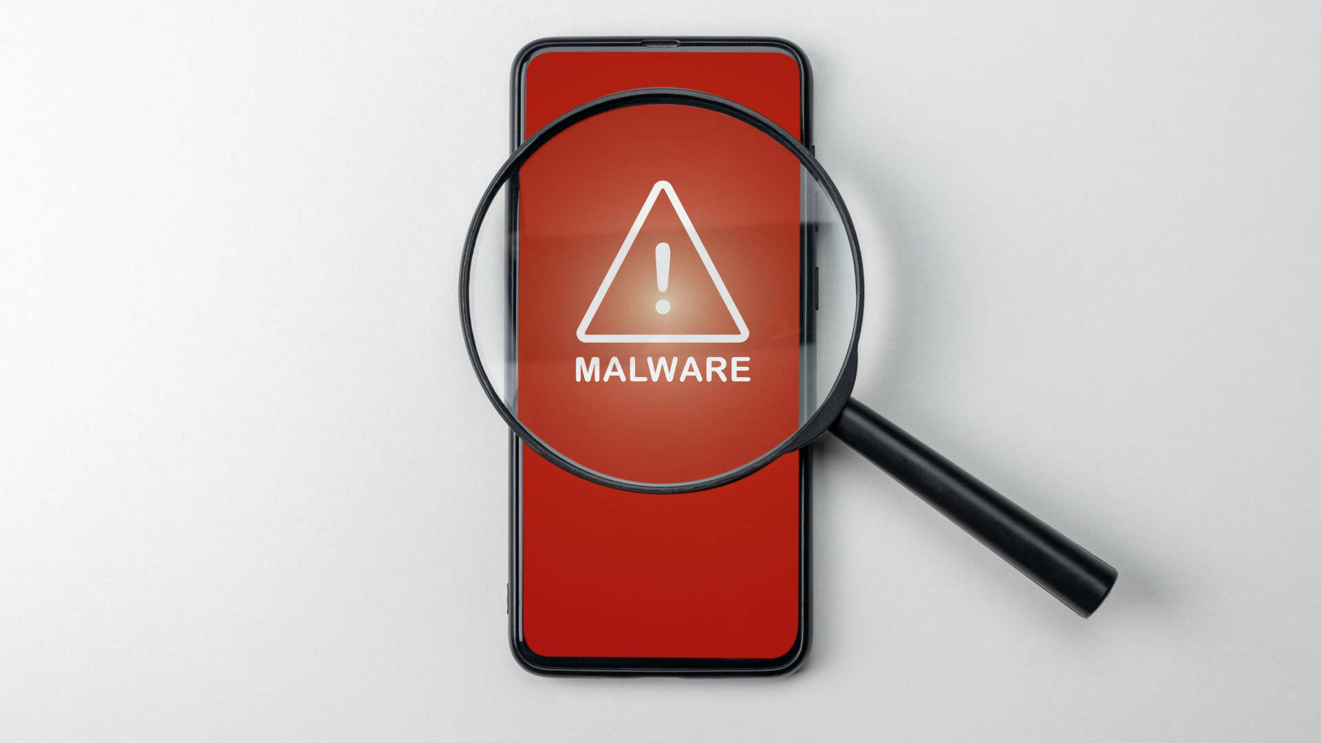 Lupa sobre celular com sinal de alerta detectando malware. Vírus sob a lente, representando aplicativo malicioso encontrado por antivírus